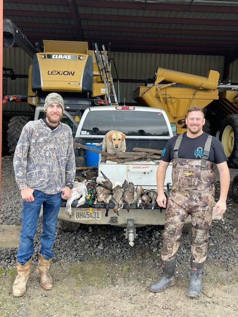 Two hunters and a dog beside a pickup in front of the farm shop after a hunt