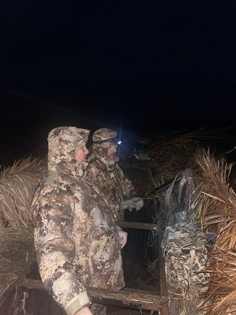 Two hunters wearing headlamps set up in the dark before shooting time