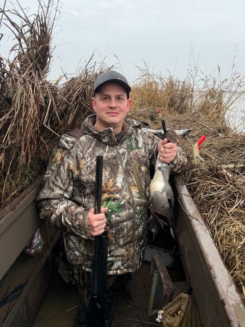 A hunter in a tule blind holds up a drake pintail