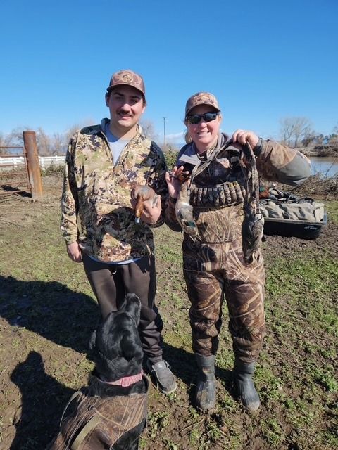 Two hunters and a black dog with their harvest on a levee